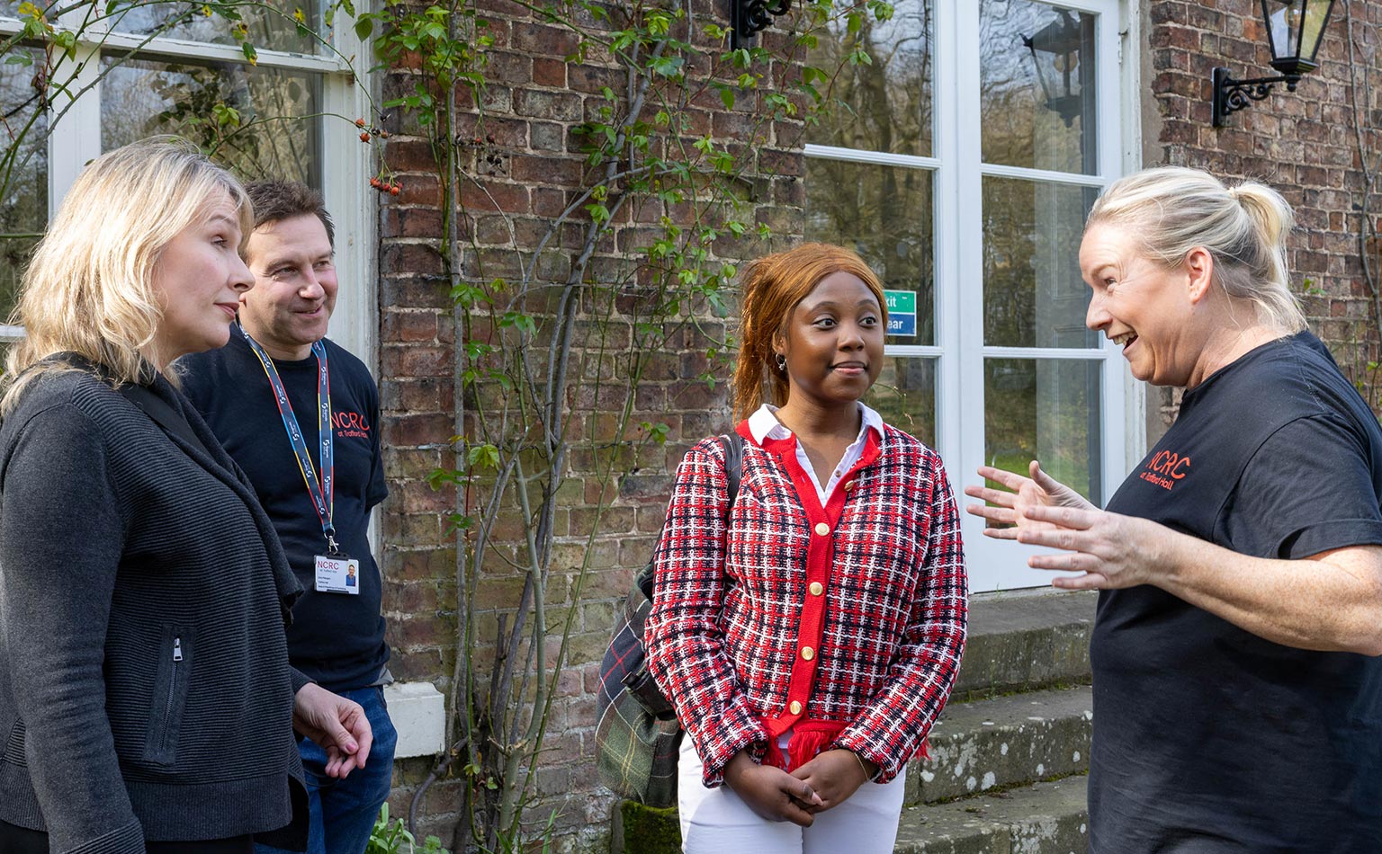 A photograph of two members of the Community Threads team standing outside Trafford Hall, having a conversation with two key partners and stakeholders