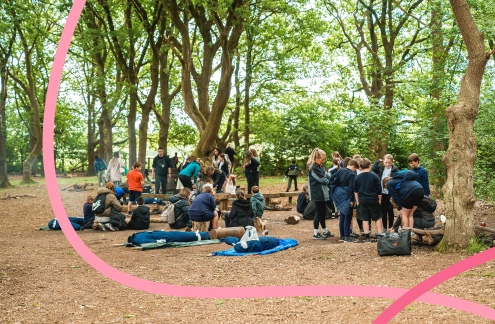 A photograph of people of various ages, gathering in a green woodland area.
